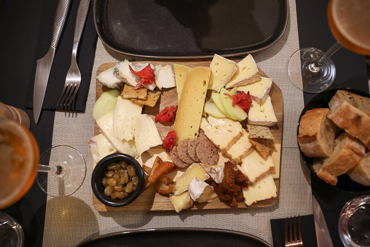 Overhead view of a Norman cheese board with Camembert, crackers, apple slices, and Calvados-soaked raisins at La Fromagerie de Bayeux