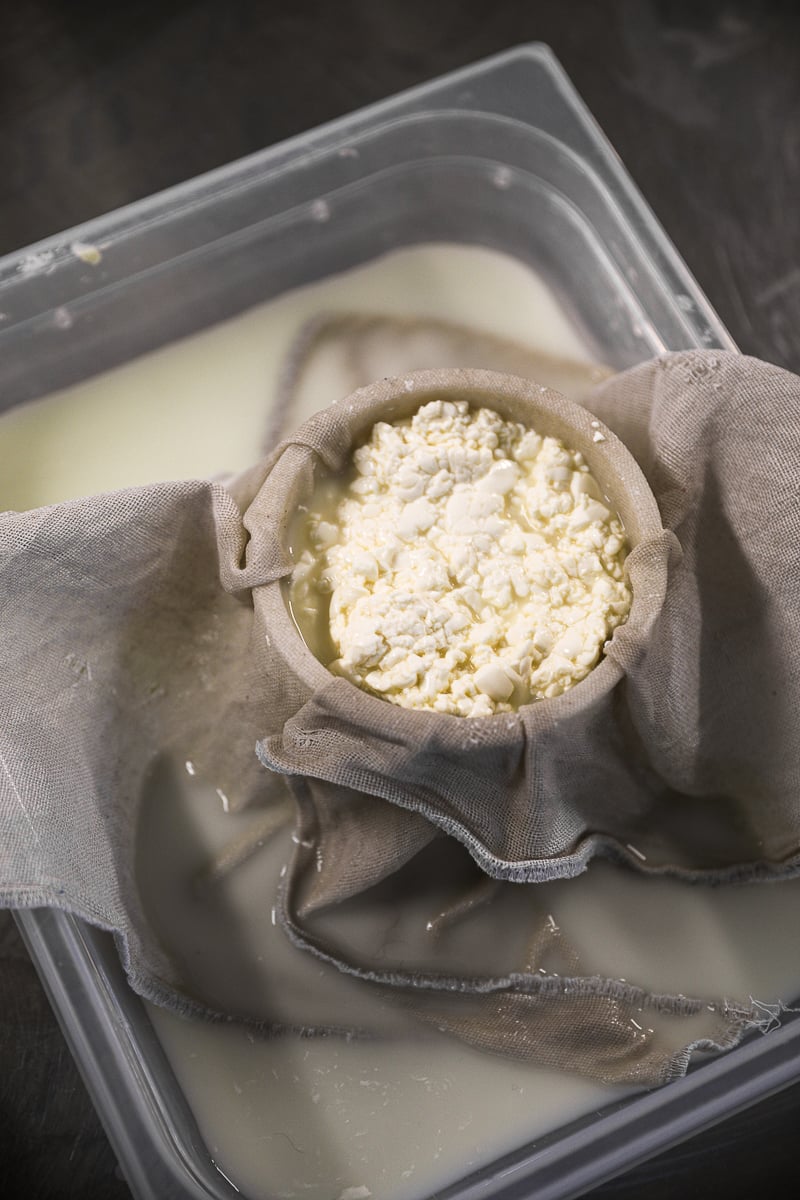 Fresh cheese curds draining in a cloth-lined mold set in a tub of whey during a Paris cheese-making class.