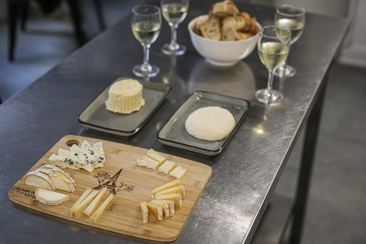 Finished cheese board with the day's handmade cheese and butter, sliced baguette, and glasses of white wine at a Paris cheese and wine tasting.