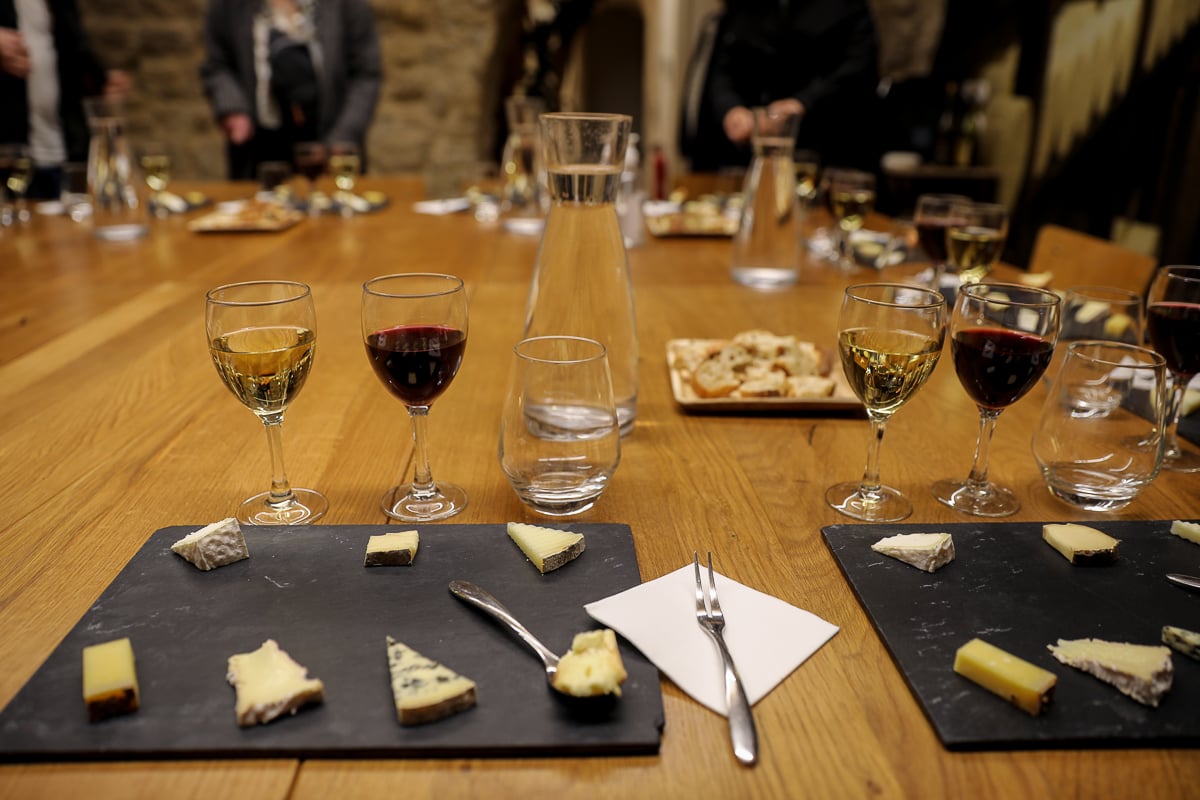 Slate boards of sliced French cheeses with glasses of red and white wine and a carafe, set up for a cheese and wine pairing in Paris.