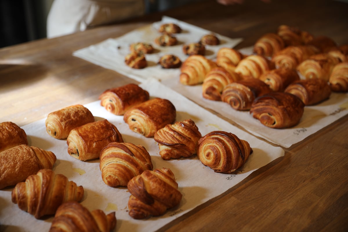 Trays of freshly baked golden croissants and pains au chocolat cooling on a wooden table.