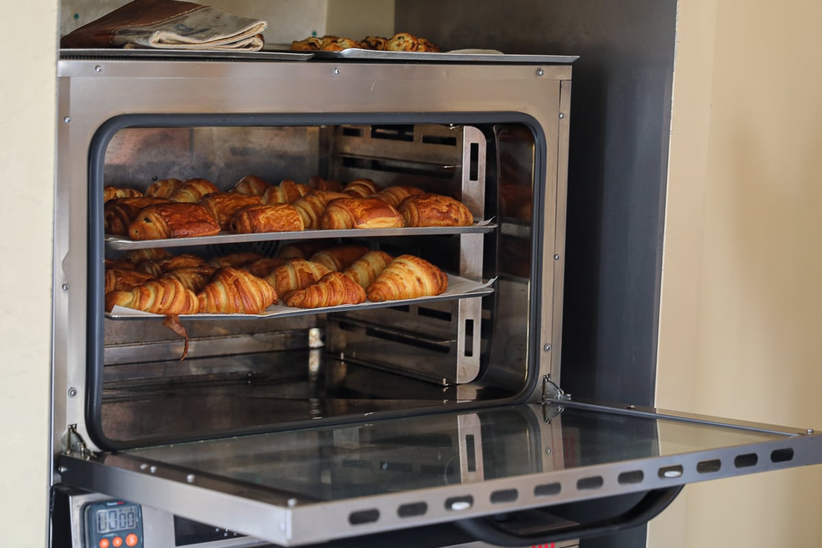 Racks of just-baked croissants and pains au chocolat inside an open professional oven.