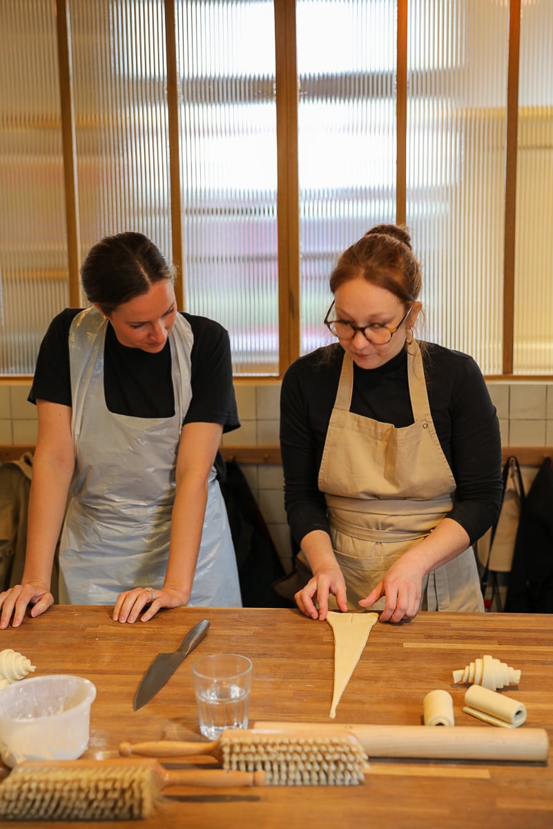 Two women in aprons shaping triangles of croissant dough together at a Paris baking class.