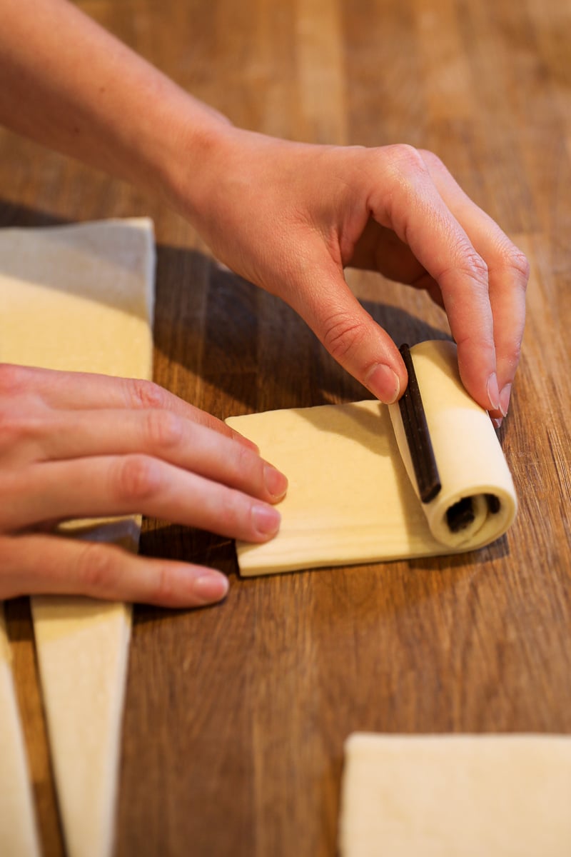Close-up of hands rolling a chocolate baton into croissant dough to form a pain au chocolat.
