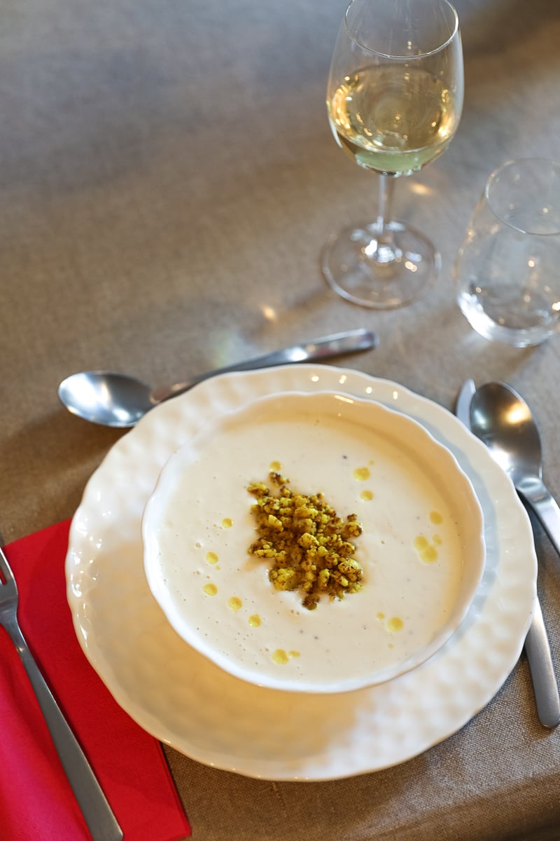 Bowl of creamy cauliflower velouté topped with curried cauliflower crumble and a drizzle of truffle oil, served with white wine.
