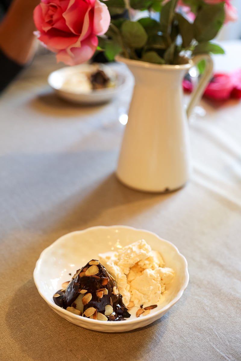 Poire Belle Hélène dessert – a poached pear coated in dark chocolate sauce and toasted almonds beside a scoop of vanilla ice cream.