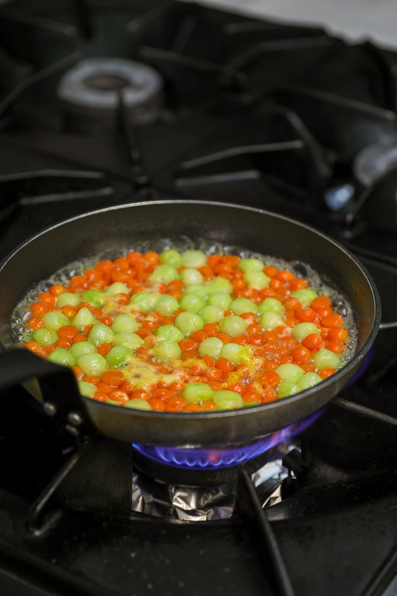 Carrot and cucumber balls sautéing in a glaze in a pan over a gas flame.