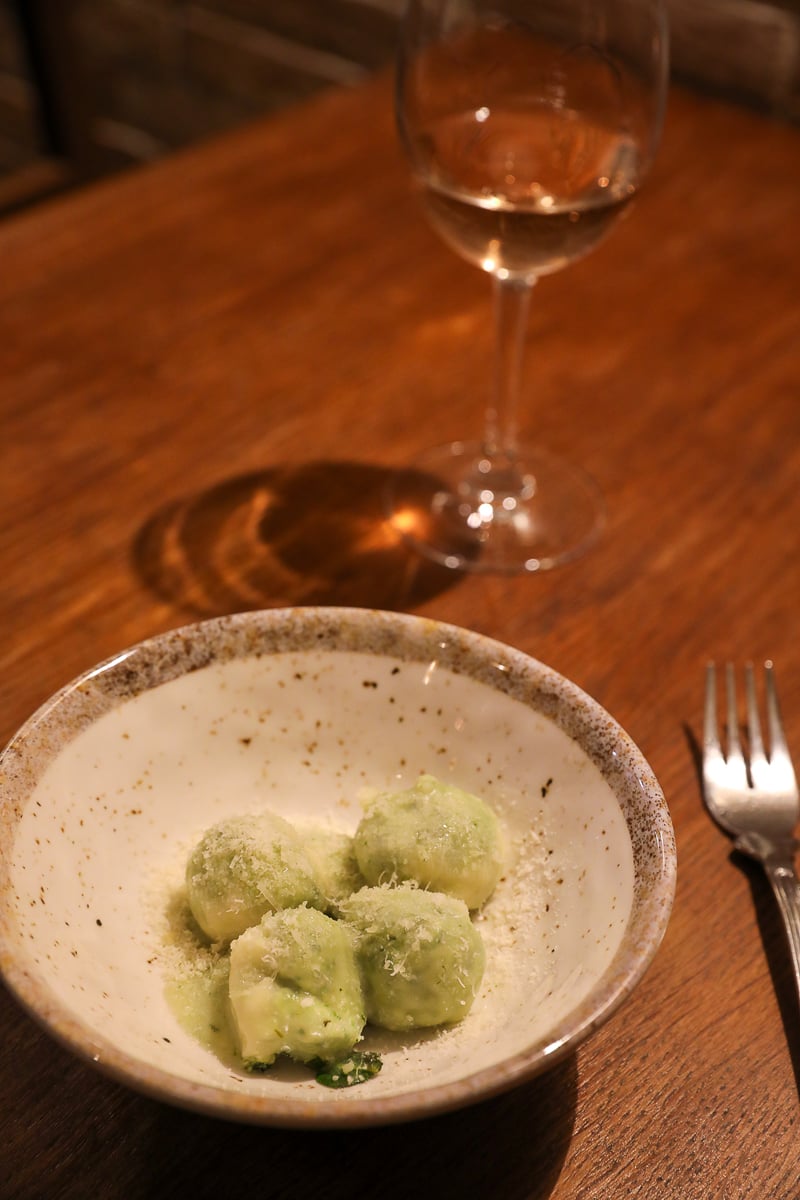 Ricotta and spinach gnudi dusted with parmesan, served alongside a glass of white wine in Florence.