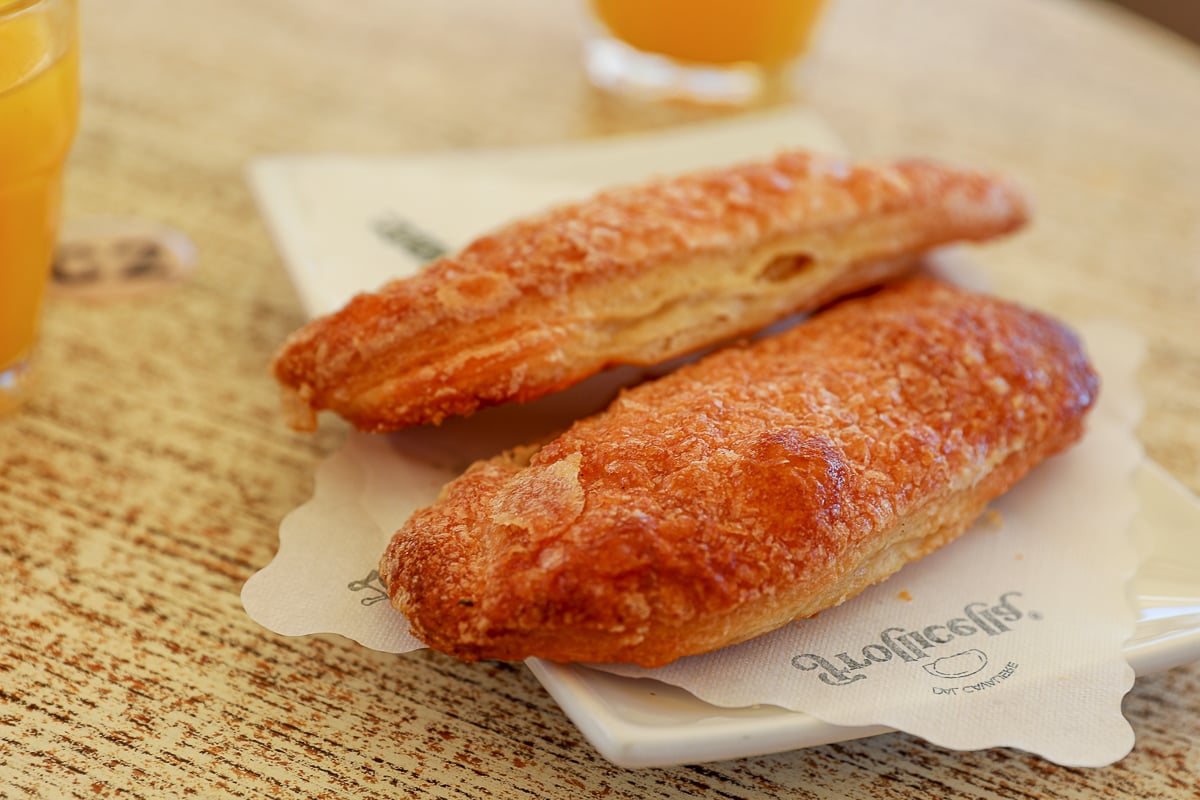 Two golden lingua di bue puff pastries with orange juice, a local breakfast treat in Procida, Italy