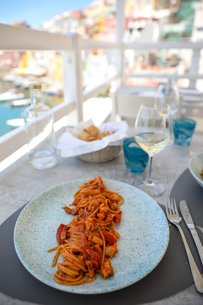 Plate of seafood pasta and a glass of white wine overlooking the harbor in Procida