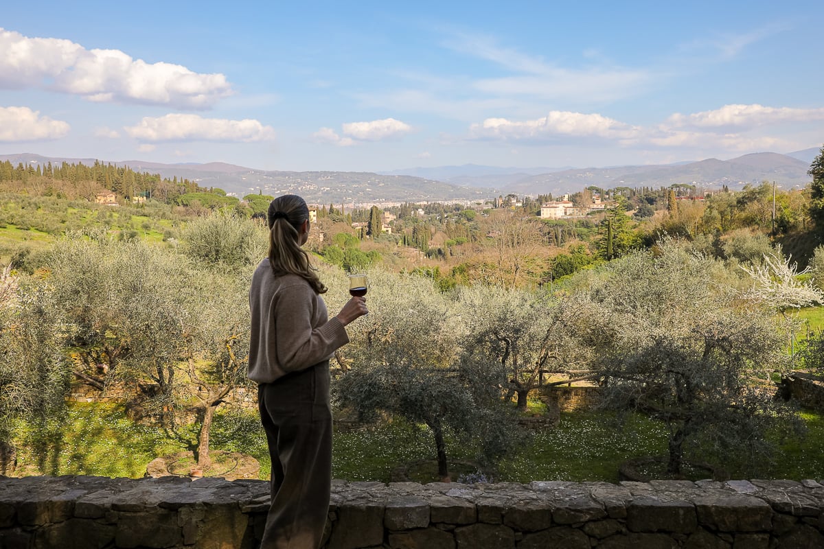 Woman holding a glass of red wine overlooking olive groves and Tuscan countryside near Florence.