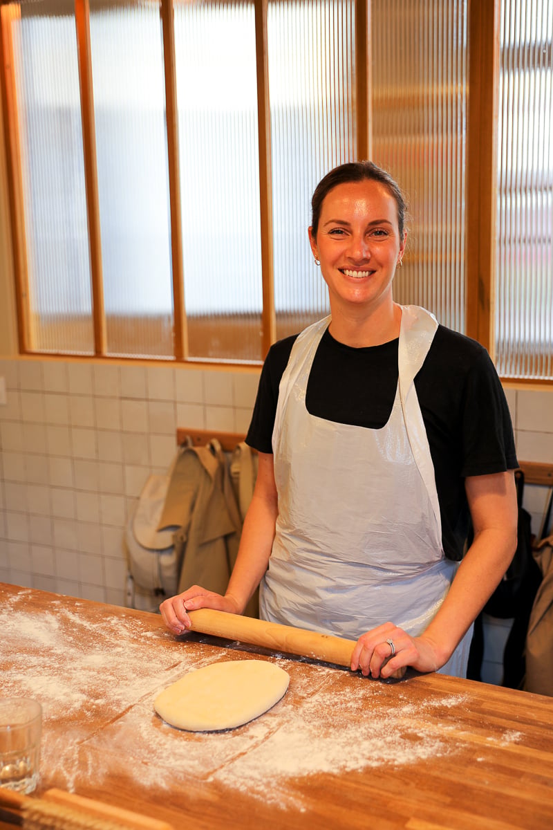 Woman in an apron smiling behind a piece of rolled-out dough at a Paris croissant baking class.