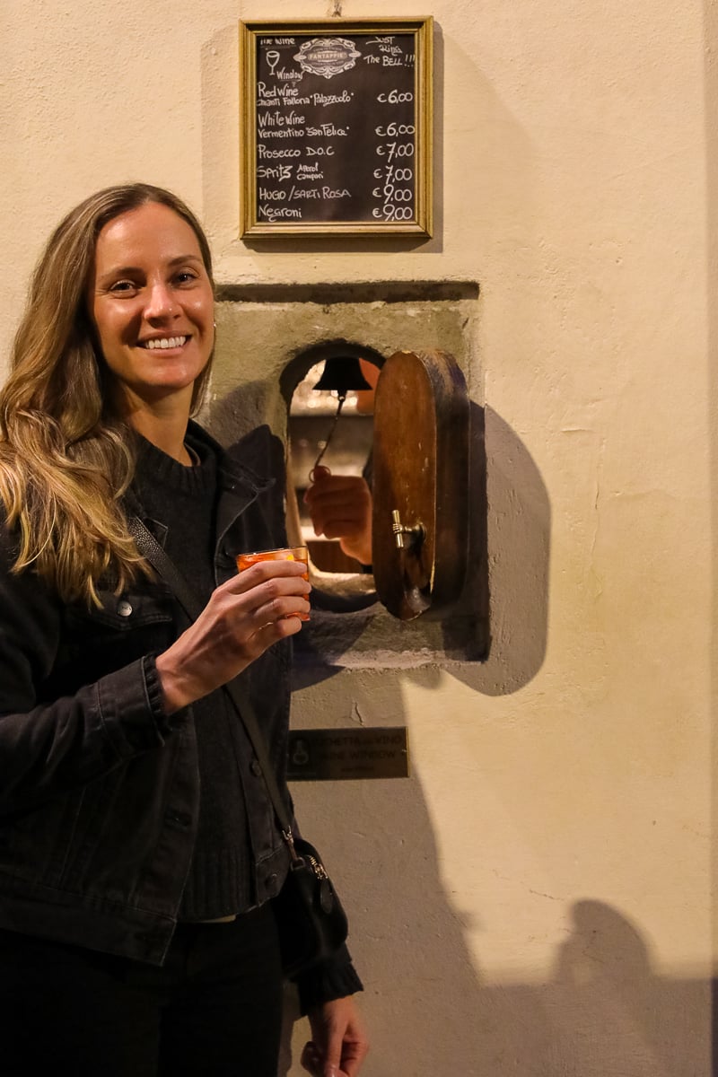 Maddy holding a negroni next to an open wine window, or buchetta del vino, in Florence.
