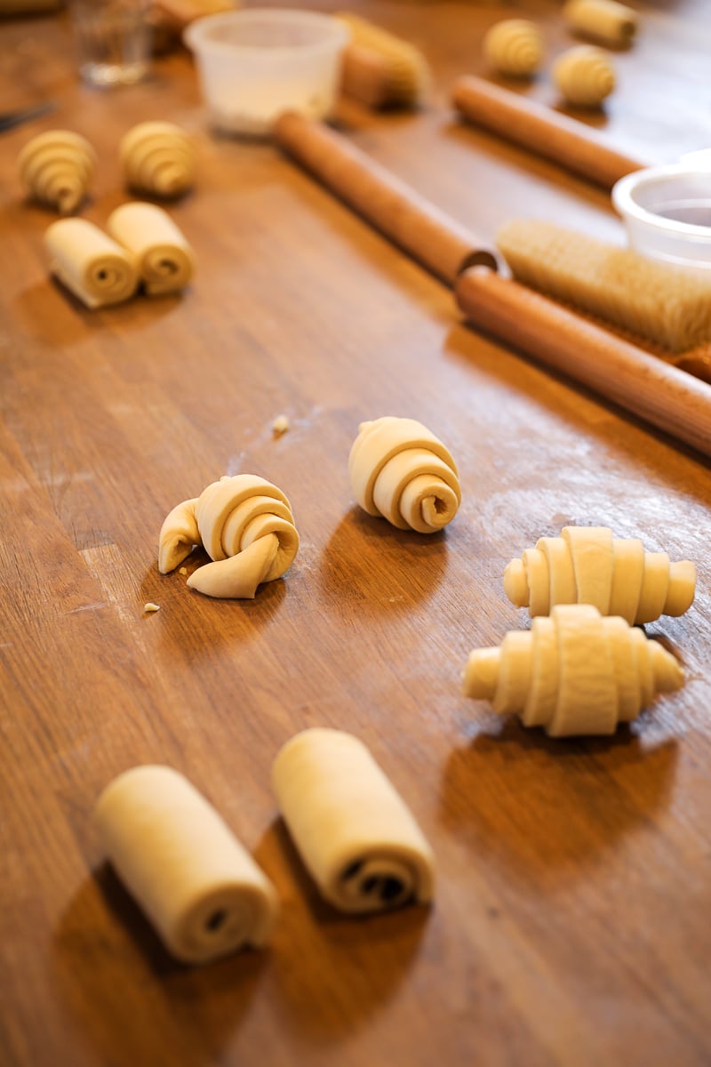 Rolled raw croissant dough in various shapes resting on a wooden table during a Paris croissant class.