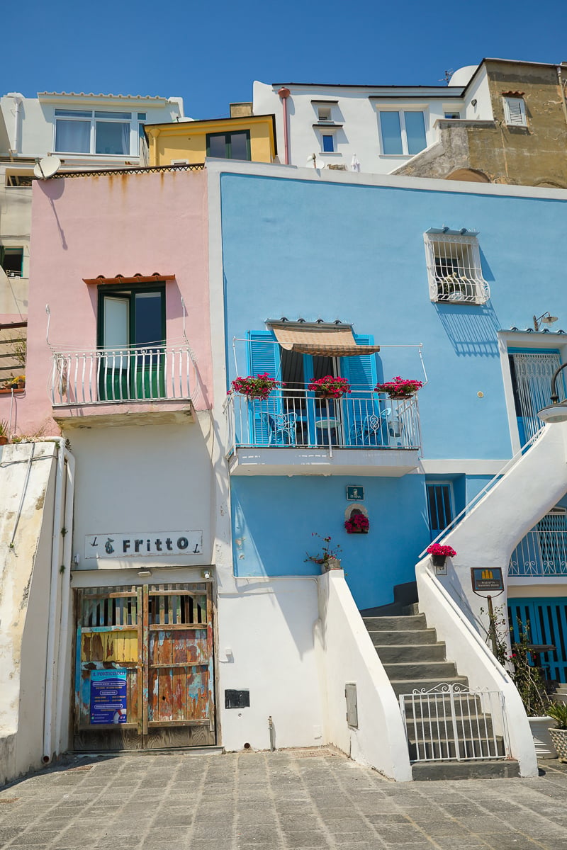 Pink and blue houses with flower-filled balconies above a fritto shop at Marina Corricella, Procida