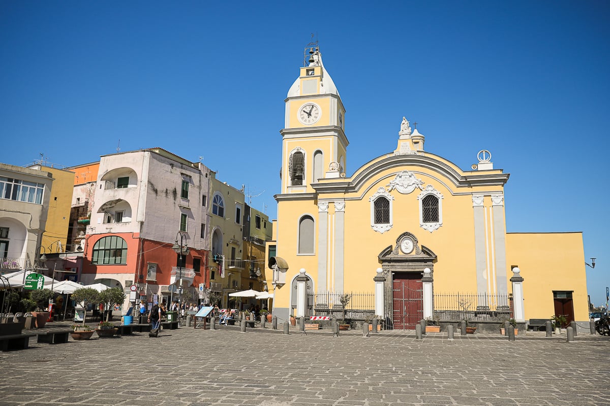 Yellow church and clock tower on the cobblestone piazza at Marina Grande, a stop on any day trip to Procida