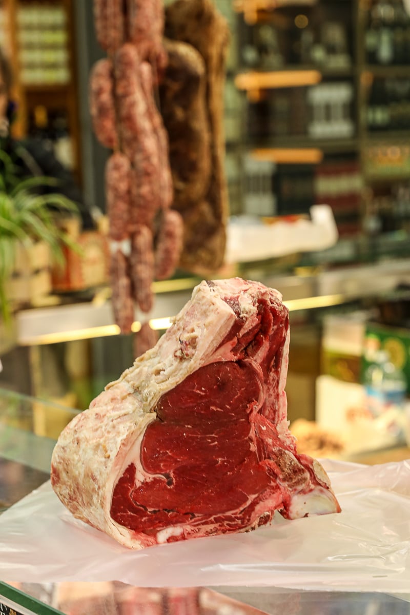 Large cut of aged Florentine beef on display at a butcher counter in Mercato Centrale.