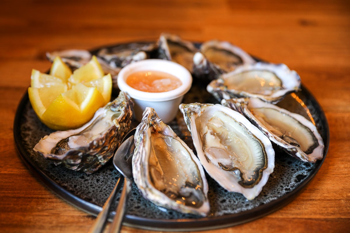 Freshly shucked Norman oysters with lemon and shallot vinegar on a dark plate, Bayeux, France