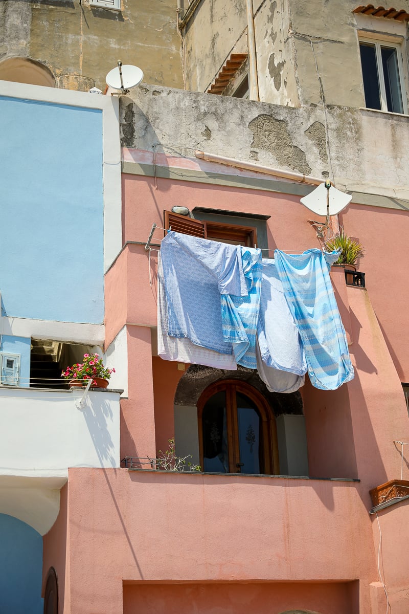 Blue linens drying on a line against a pink house facade, a typical street scene in Procida, Italy
