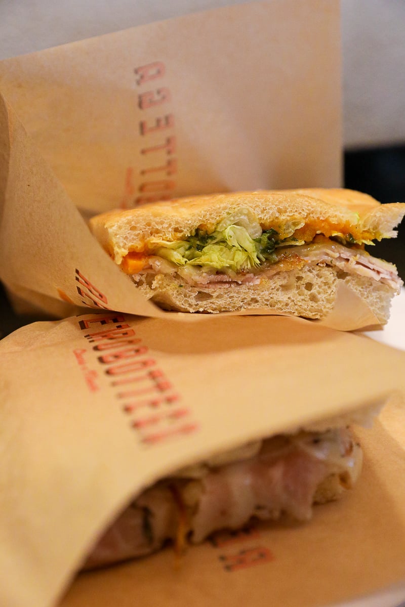 Schiacciata sandwiches wrapped in branded paper from Retrobottega, filled with prosciutto, cheese, and greens.