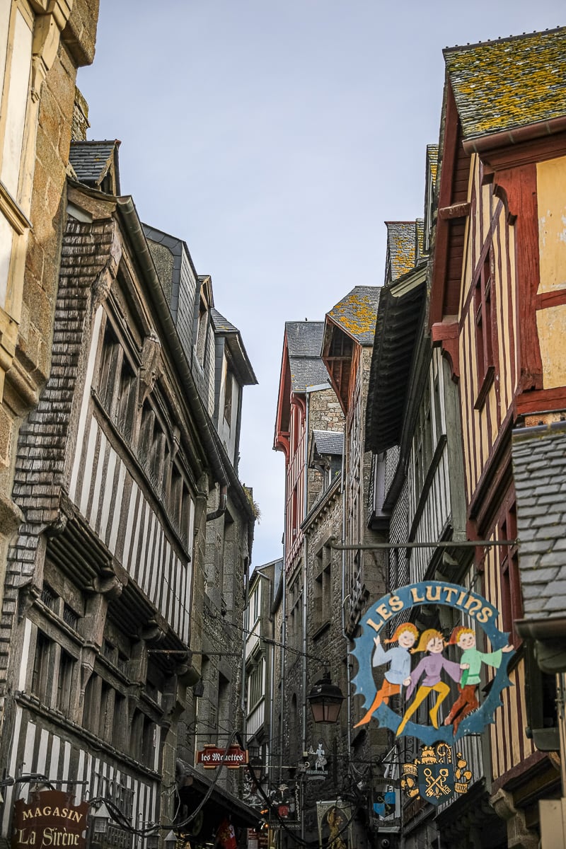 Narrow medieval lane lined with half-timbered buildings and shop signs inside the village of Mont Saint-Michel