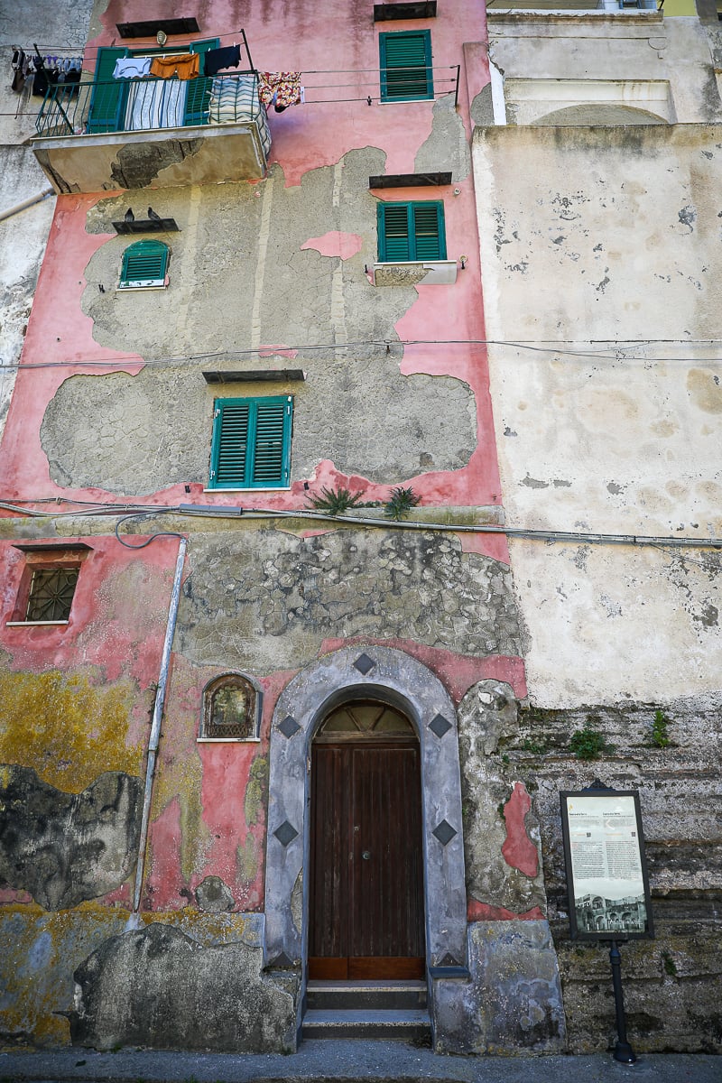 Weathered pink facade with green shutters and laundry on a balcony in Terra Murata
