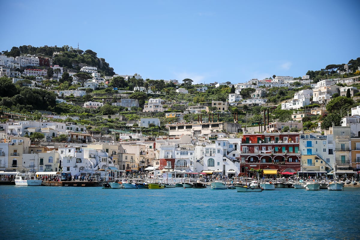 Marina Grande harbor in Capri, with fishing boats moored along the dock and pastel buildings climbing the hillside behind. Capri is one of the best day trips from Naples by boat or ferry.