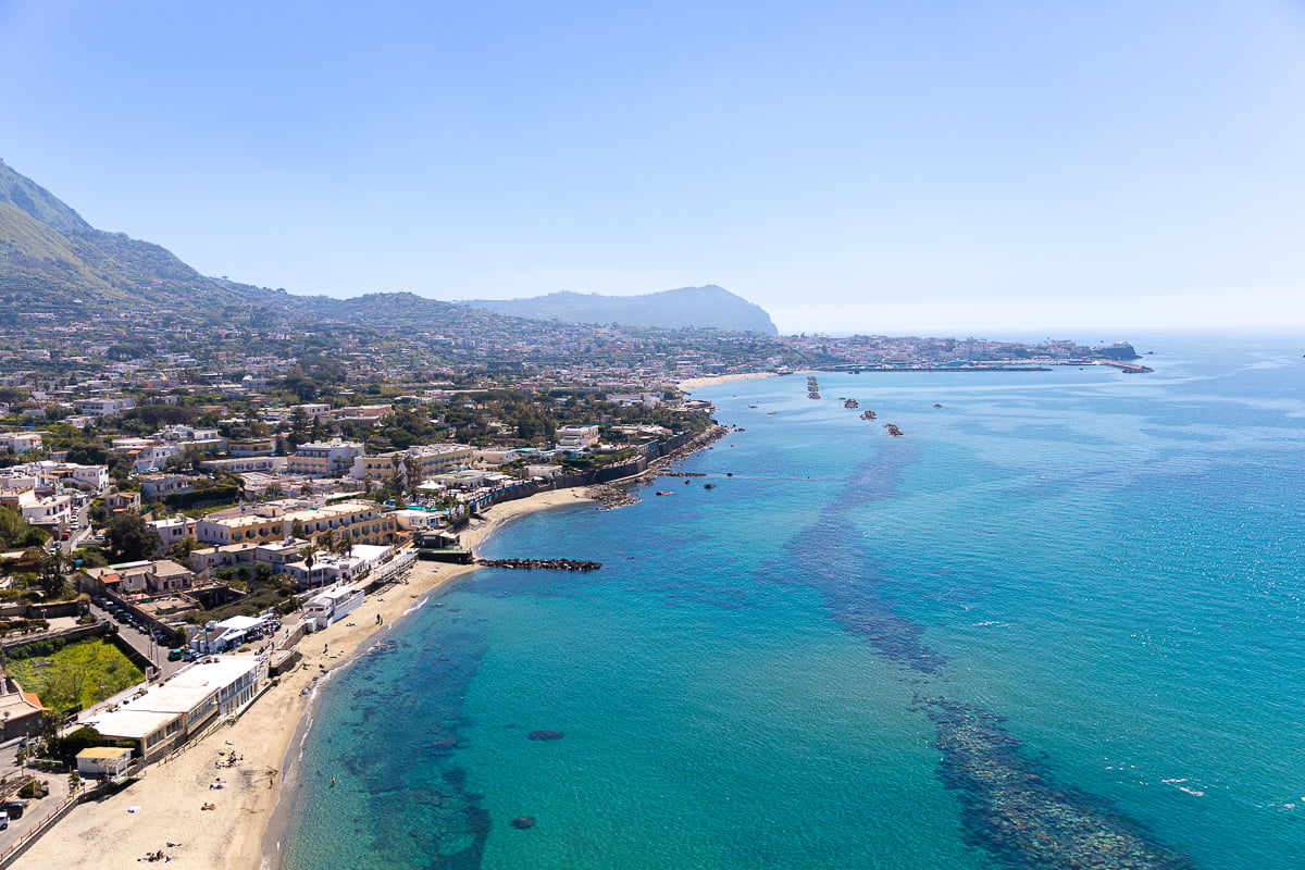Aerial view of Ischia's curved coastline and turquoise water, a relaxing island day trip from Naples