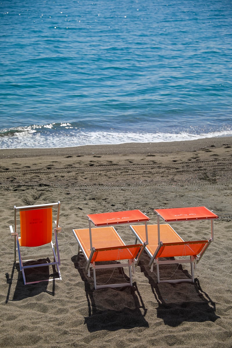 Empty orange folding beach chairs and loungers set on a sandy shore beside gentle waves in Ischia