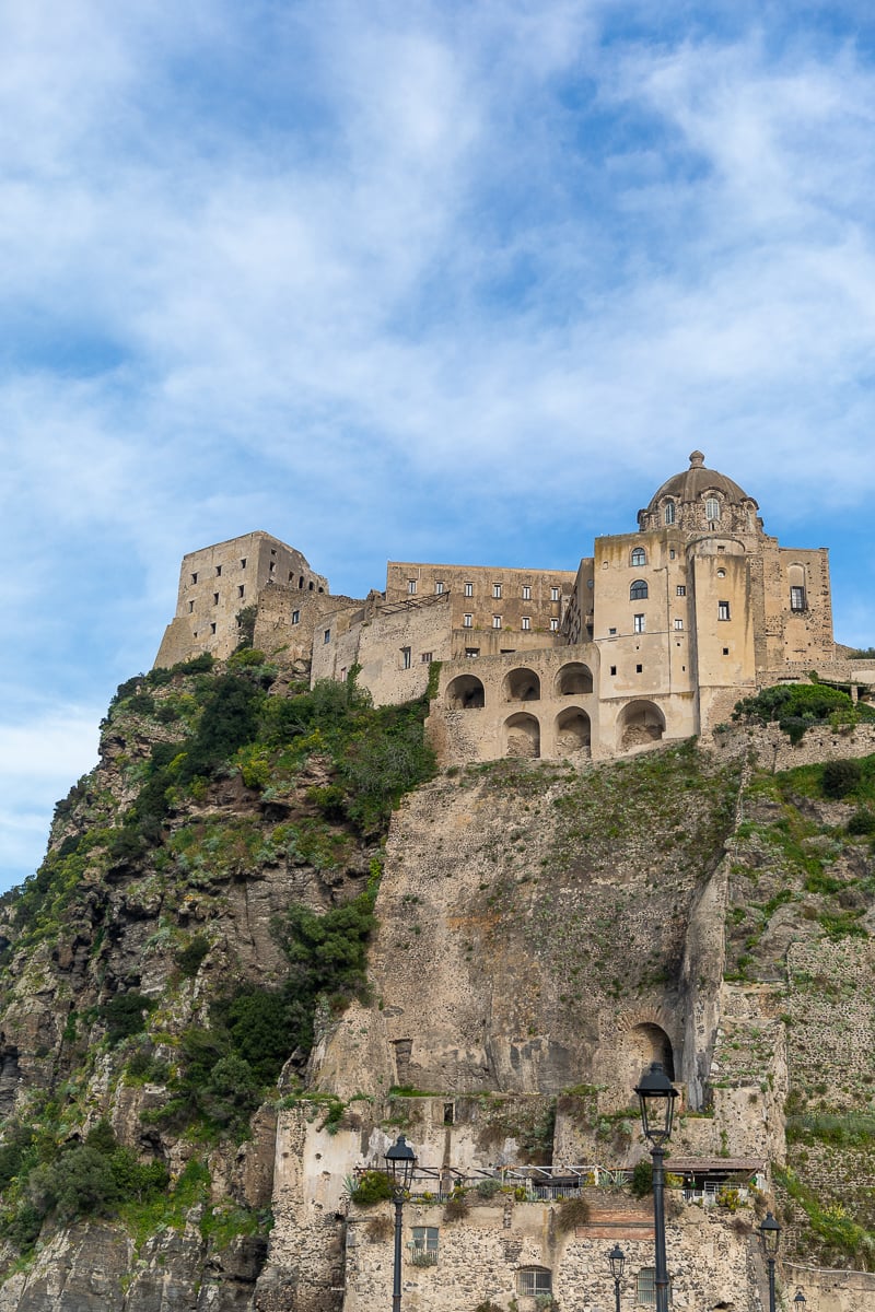 Aragonese Castle's stone walls and domed rooftops perched atop a rocky islet, connected to Ischia by a stone bridge