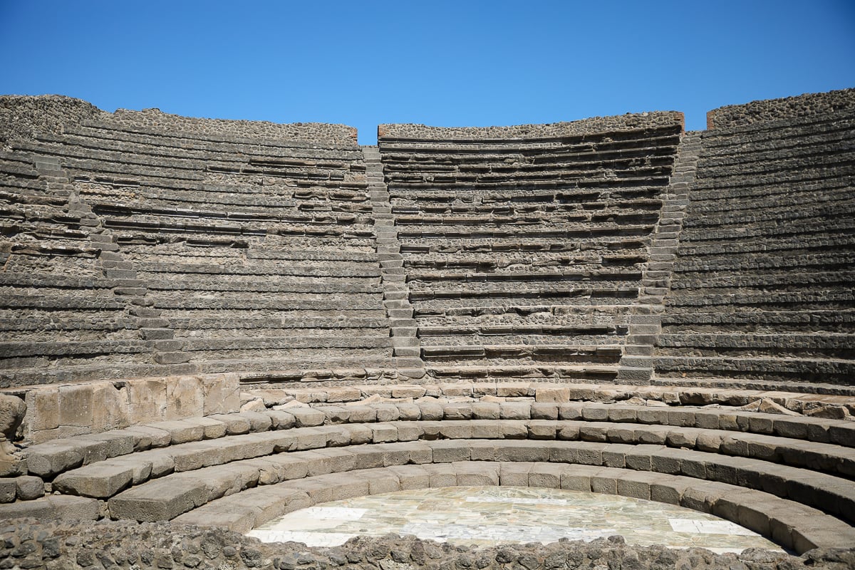 Weathered stone steps of Pompeii's small theater, with a circular marble-inlaid stage floor in the foreground