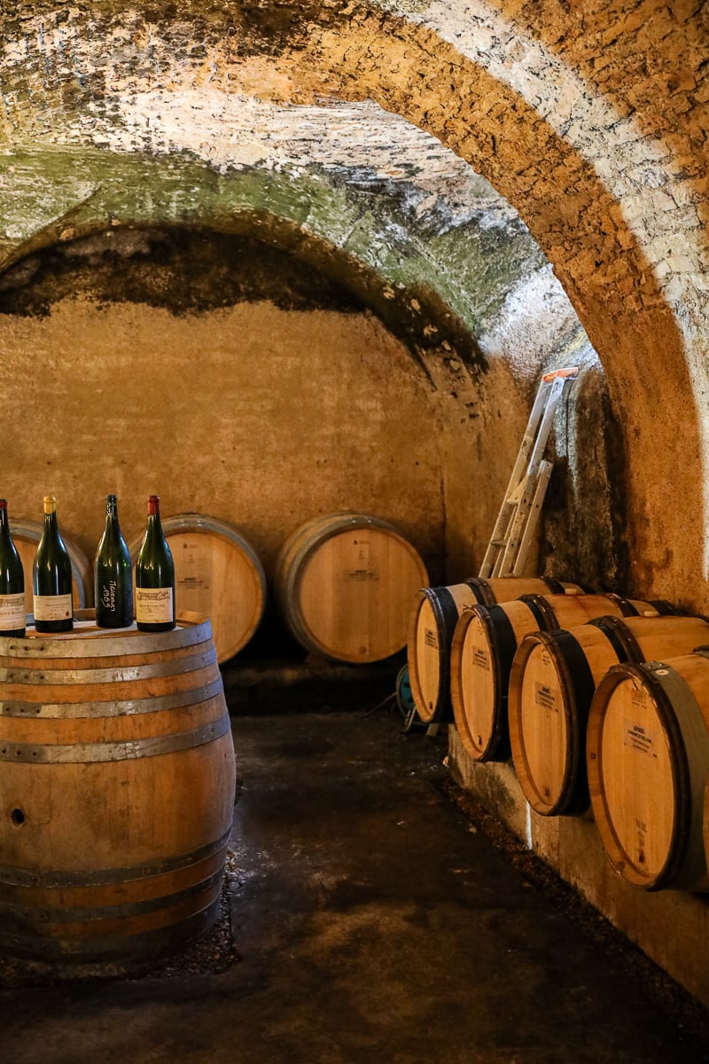 Historic Burgundy wine cellar with vaulted stone ceilings, oak barrels, and bottles ready for tasting