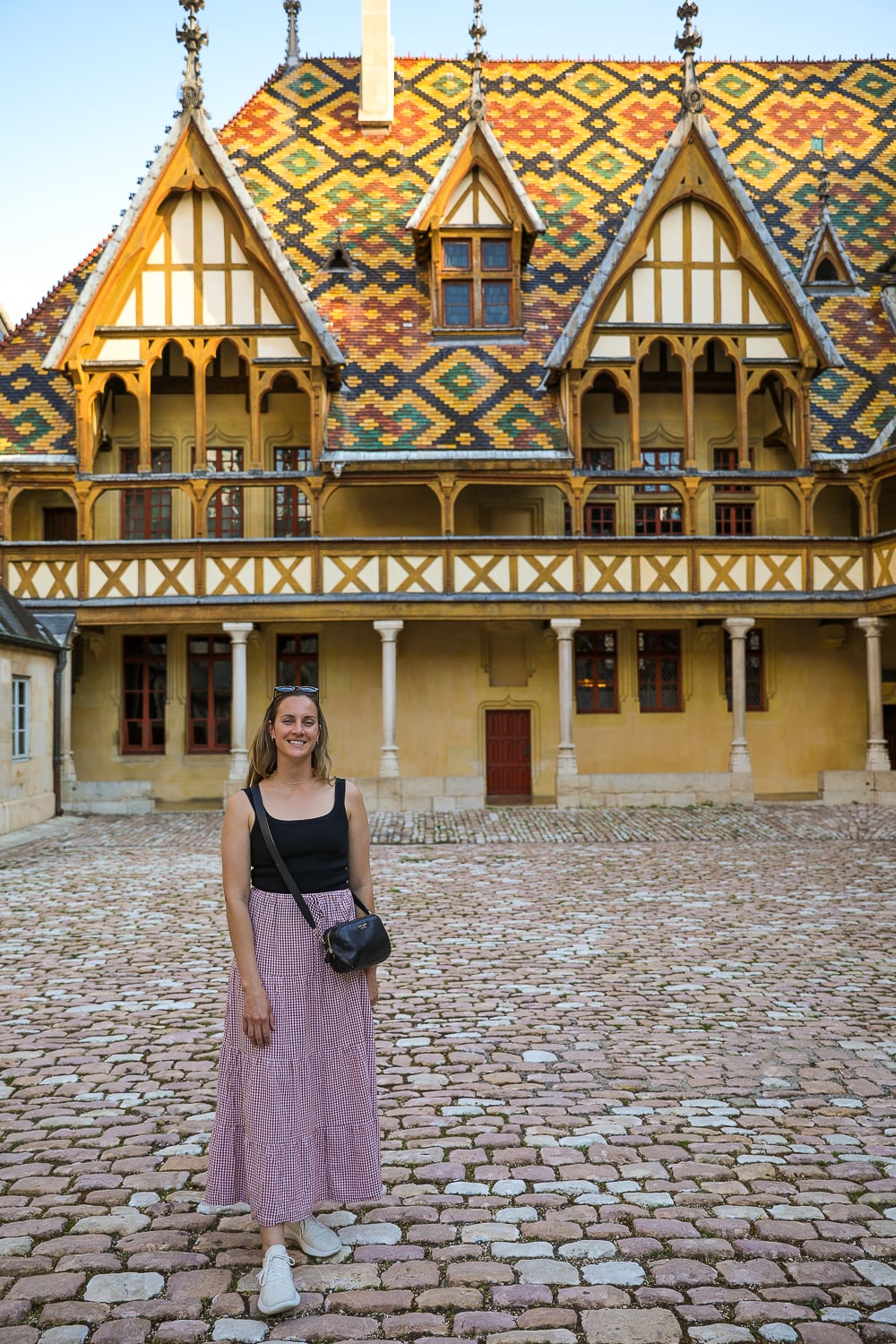 Woman standing in the courtyard of the Hôtel-Dieu in Beaune beneath its colorful glazed-tile roof