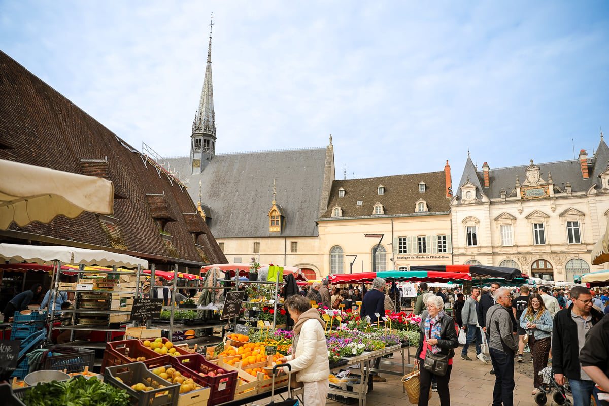 Busy Beaune Saturday market with flower and produce stalls surrounded by historic Burgundy architecture