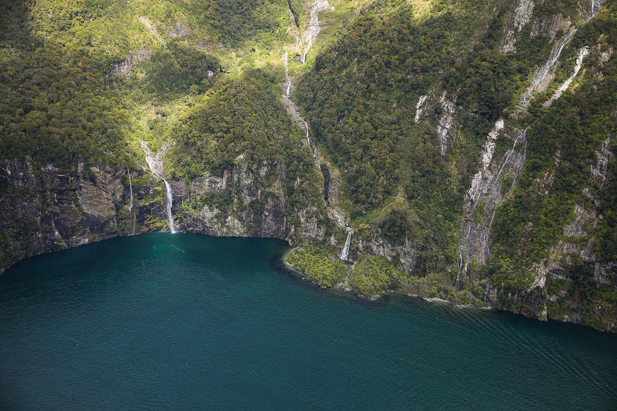 Aerial view of waterfalls cascading from rainforest-covered cliffs into the deep blue waters