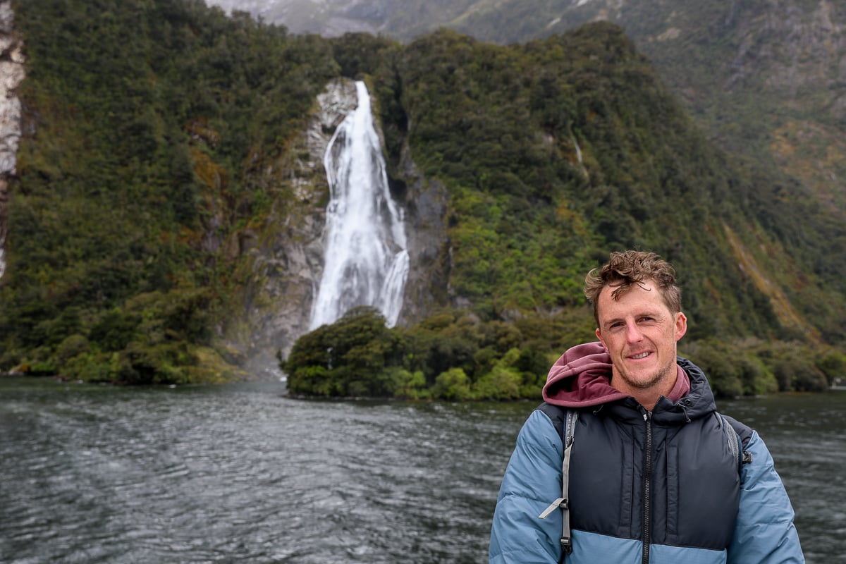 Traveler on a Milford Sound cruise with Bowen Falls cascading down the mountainside behind him