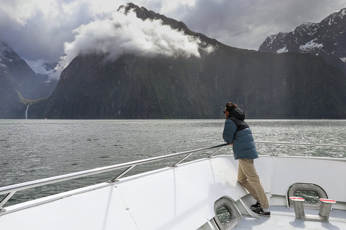 Traveler taking in mountain and waterfall views from the bow of a cruise boat