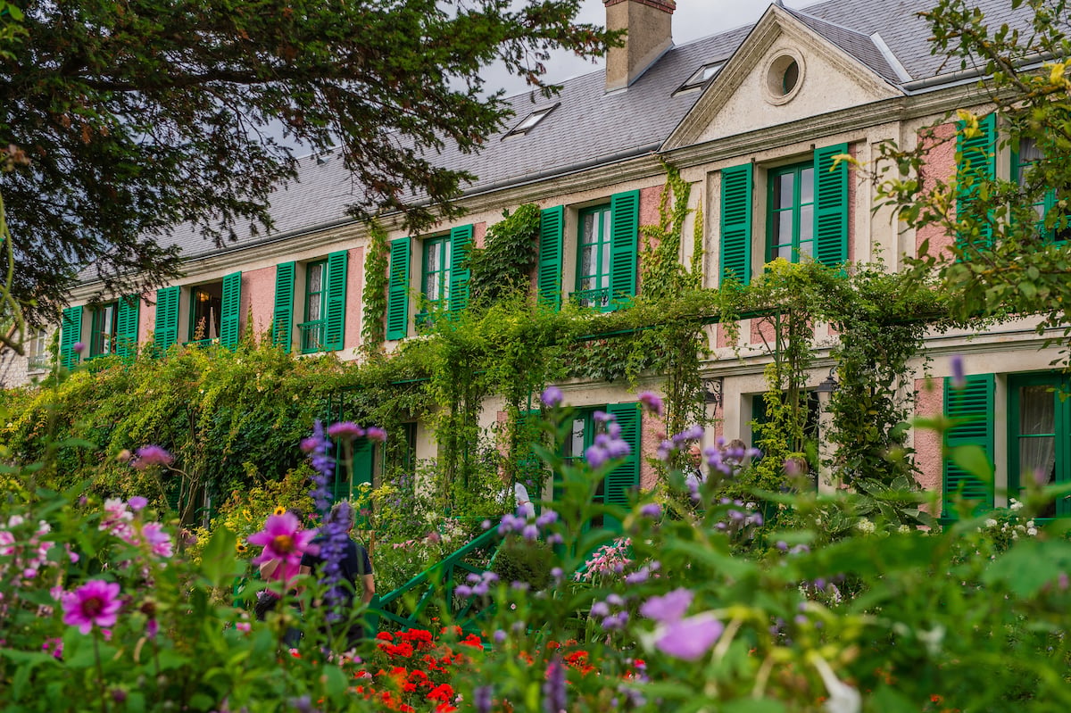 A vibrant scene at the pink home of Claude Monet in Giverny, where visitors walk through dense, colorful flower gardens that make for one of the most beloved day trips from Paris.