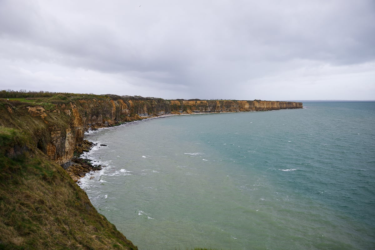 Dramatic view of the limestone cliffs at Pointe du Hoc in Normandy, France, overlooking the Atlantic Ocean on a cloudy day.