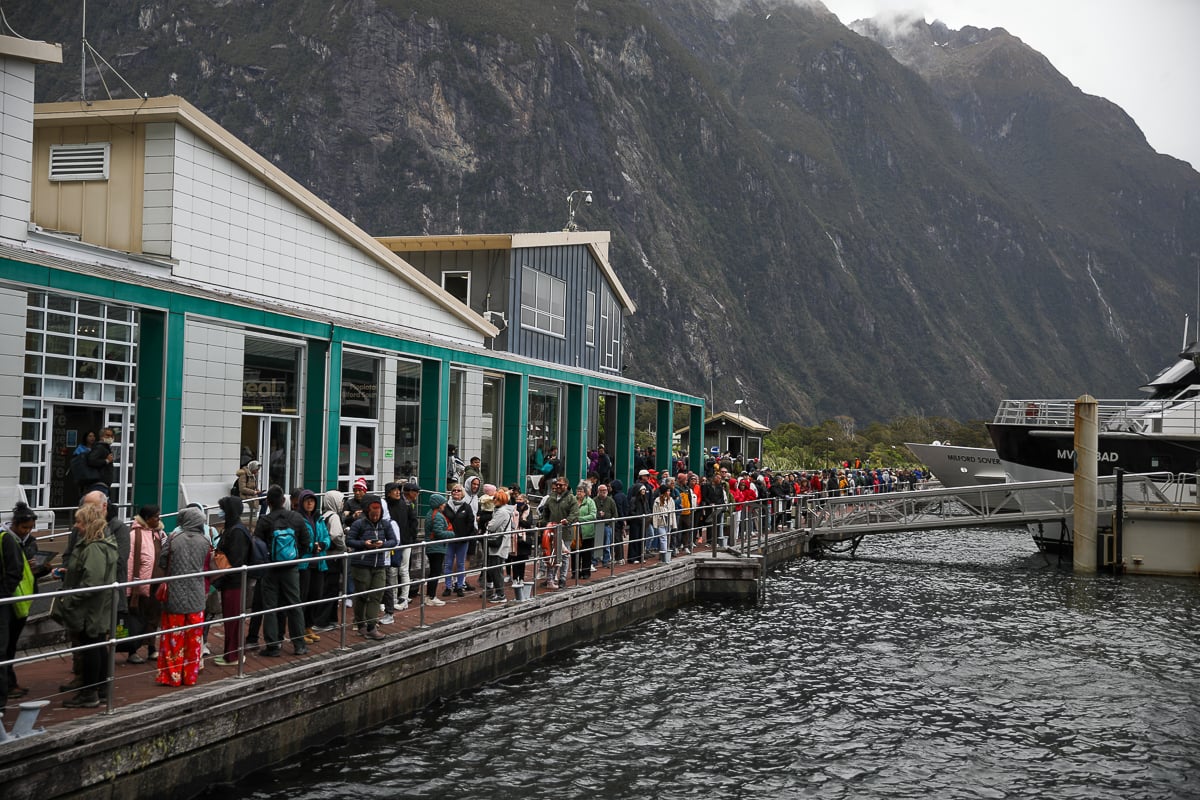 Visitors lining up to board a fjord cruise boat at the terminal beneath towering mountains