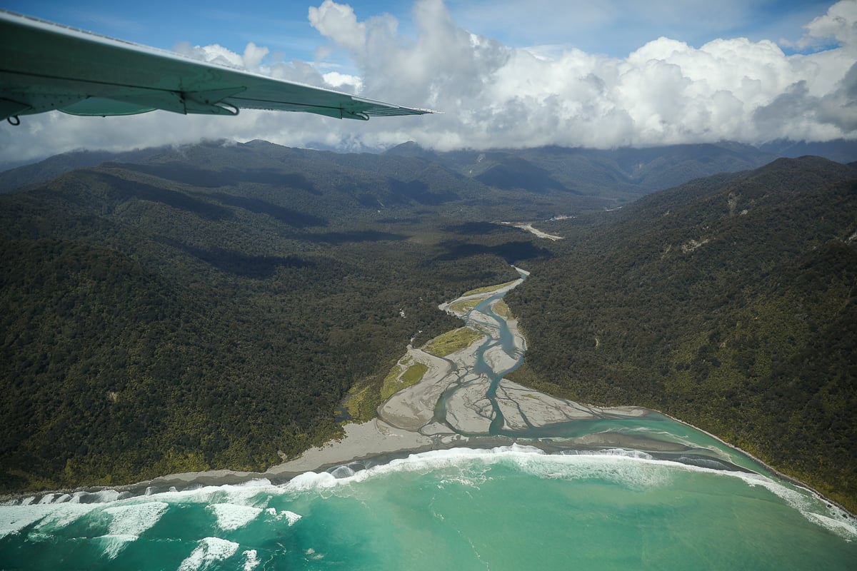 Aerial view of a turquoise river meeting the western coast of the South Island of New Zealand during a scenic flight