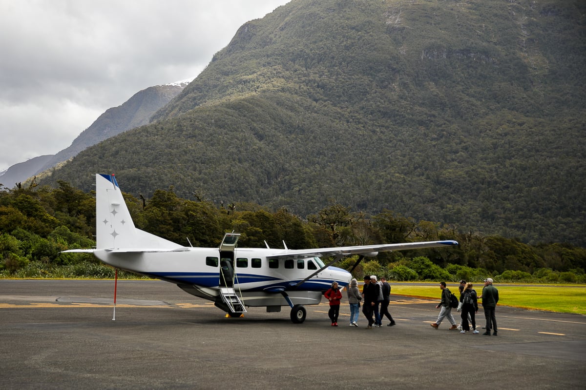 Scenic plane at Milford Sound Airport with passengers boarding beneath forest-covered mountains