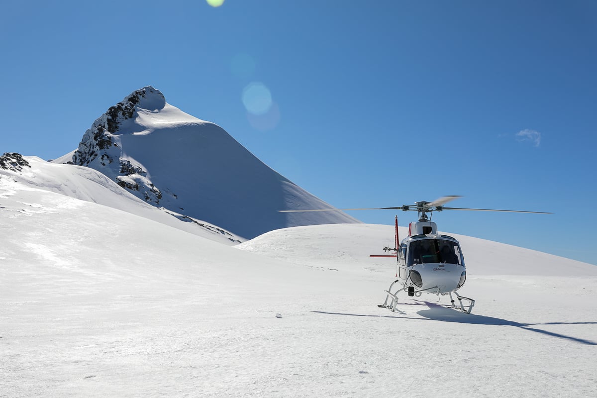 Helicopter parked on a snowy alpine glacier during a scenic flight near Milford Sound, New Zealand