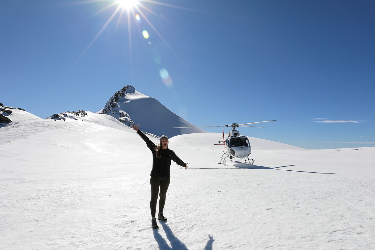Woman beside a helicopter on a snowy mountain landing during a New Zealand helicopter tour