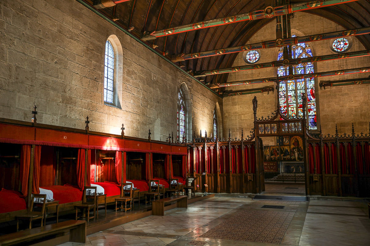 Historic hospital ward with red-canopied beds and stained-glass windows inside the Hôtel-Dieu - one of the best things to do in Beaune, France