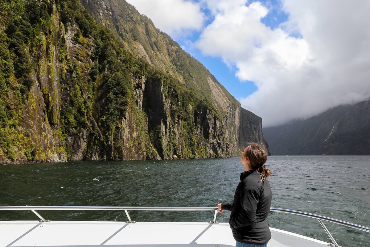 Woman admiring towering cliffs and waterfalls from the bow of a Milford Sound cruise boat