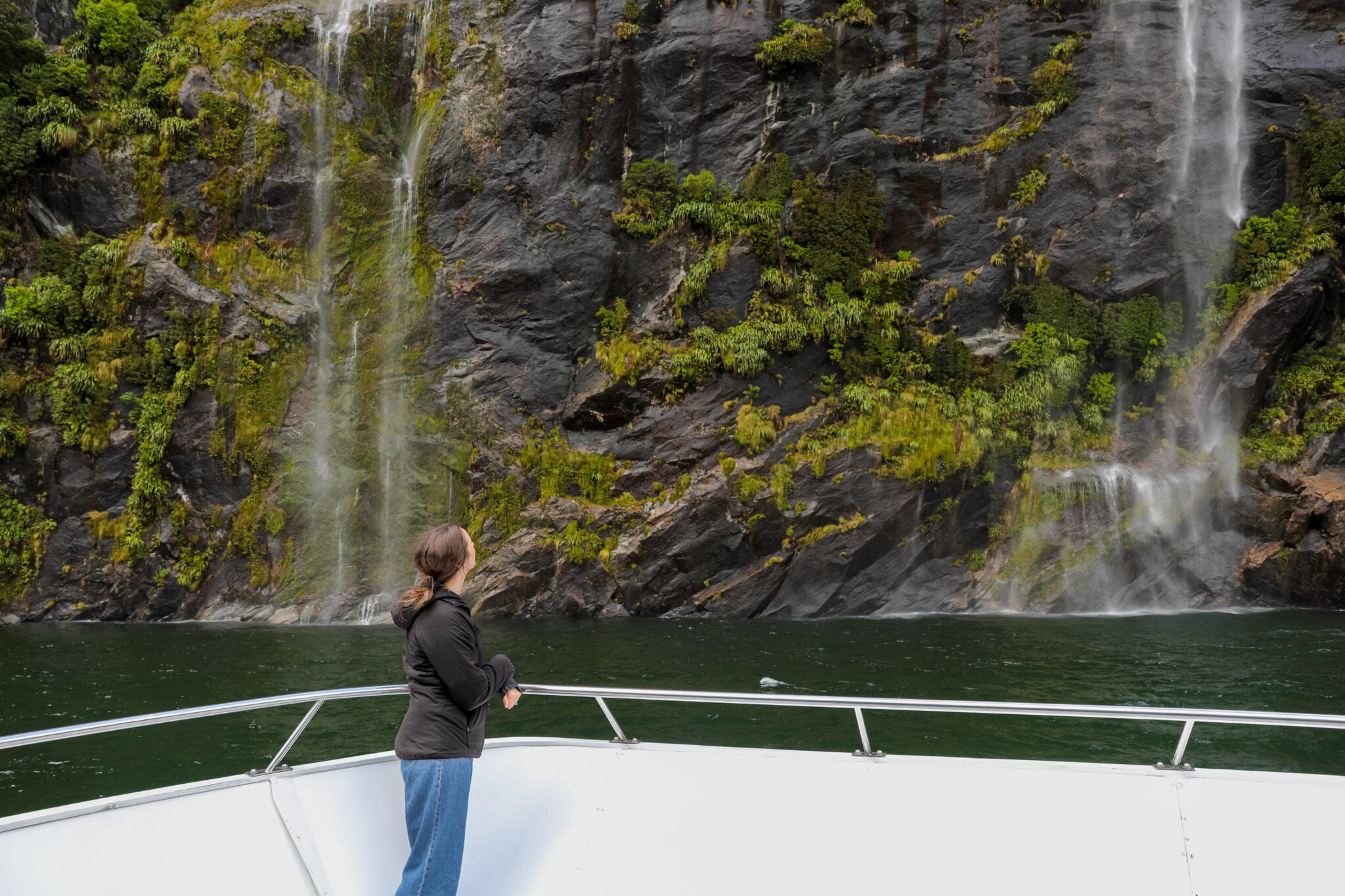 Woman watching waterfalls cascade down a rocky cliff from the bow of a fjord cruise boat