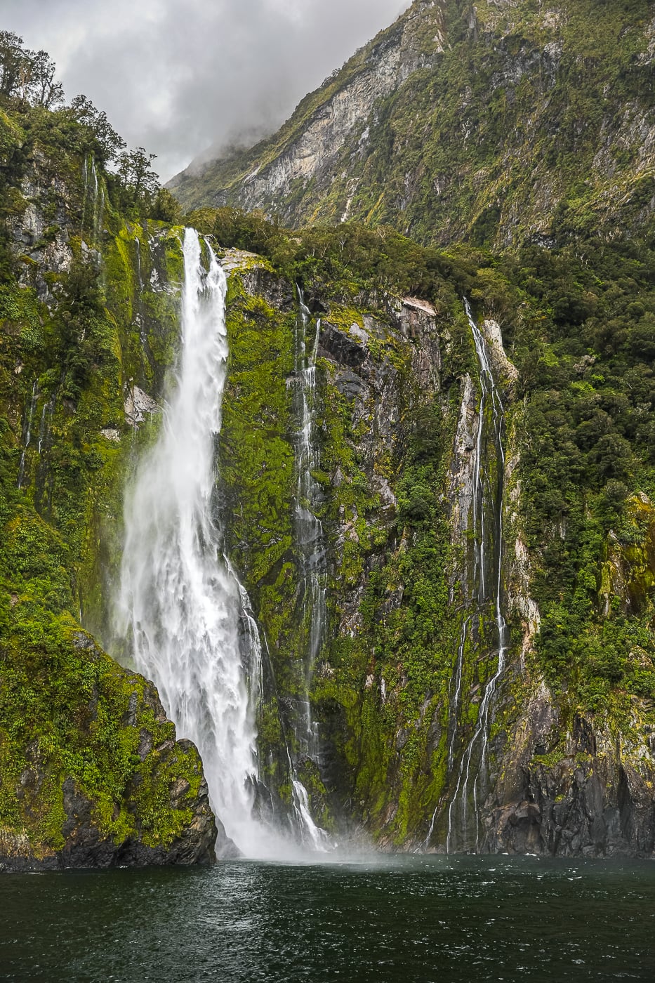 Powerful Bowen Waterfall cascading down a moss-covered cliff into Milford Sound, New Zealand