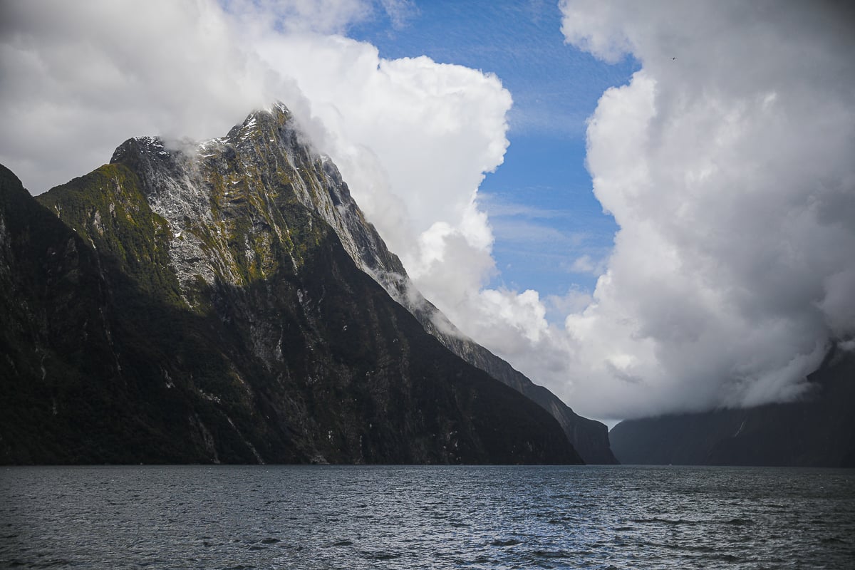 Dramatic mountain peaks and towering clouds reflected over the dark waters of Milford Sound