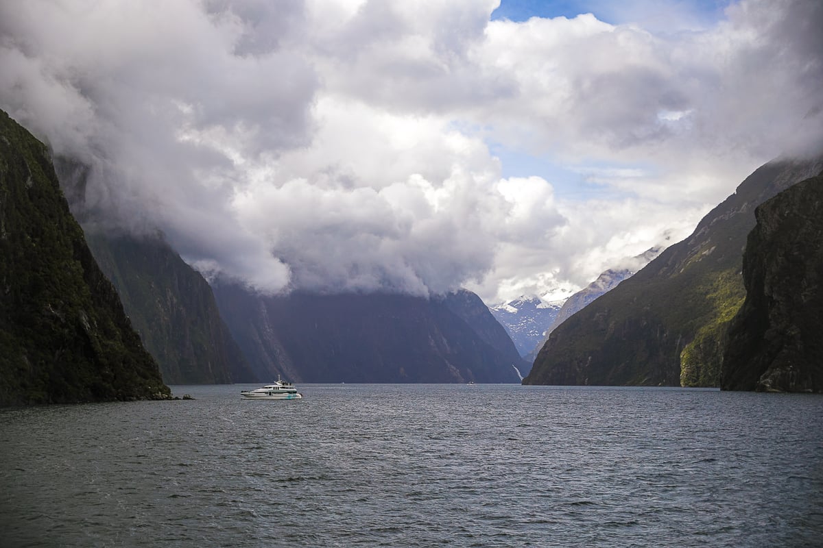 Cruise boat sailing through a fjord beneath dramatic cloud-covered mountains